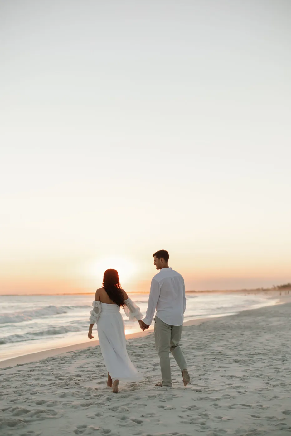 Casal de mãos dadas caminhando na areia em direção ao sol