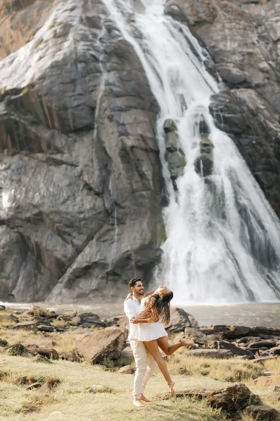 Casal rindo, ela no colo dele, diante da cachoeira