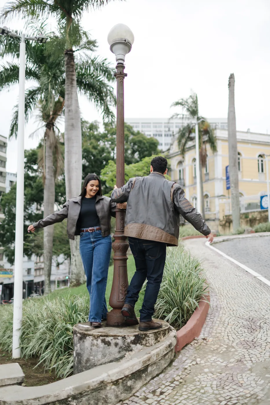 Casal brincando de equilíbrio no poste antigo da praça