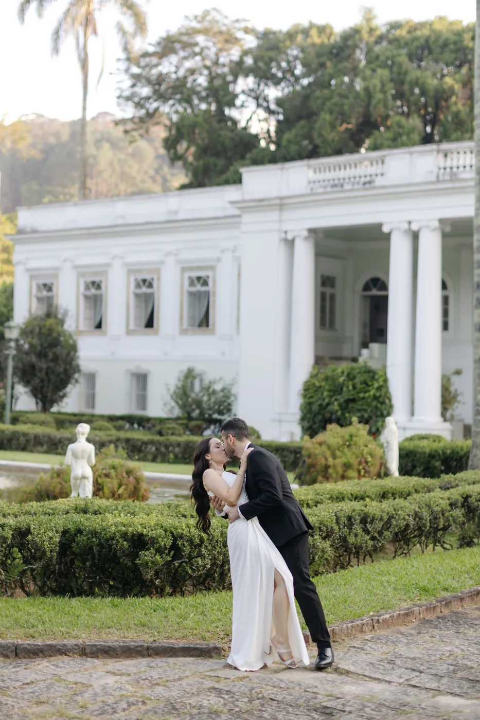 Casal se beijando no jardim, com o casarão ao fundo