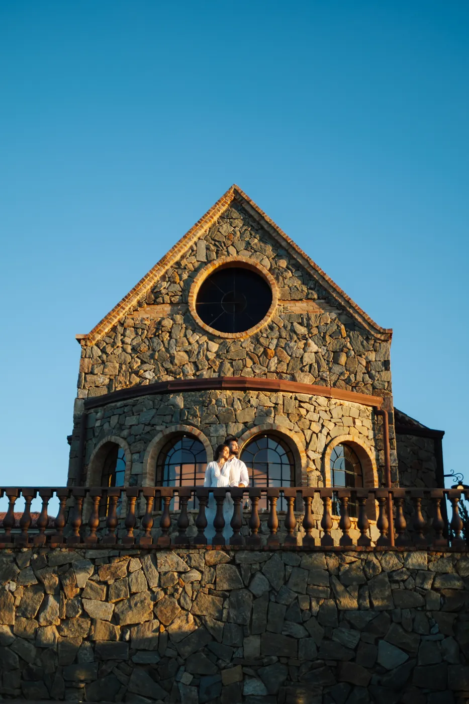 Casal na varanda da capela de pedra, na luz dourada