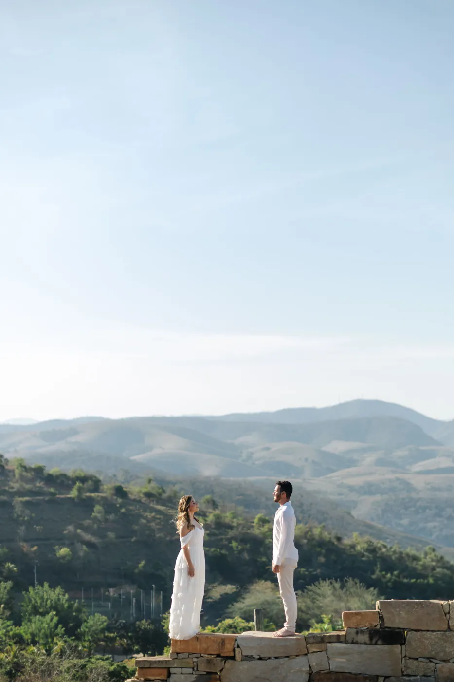 Casal frente a frente sobre um muro de pedra, com vista para as montanhas