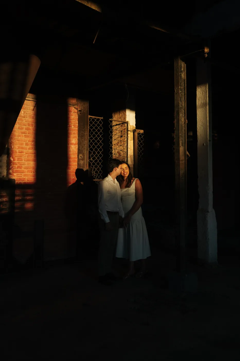 Casal iluminado por um feixe de luz dentro do galpão escuro